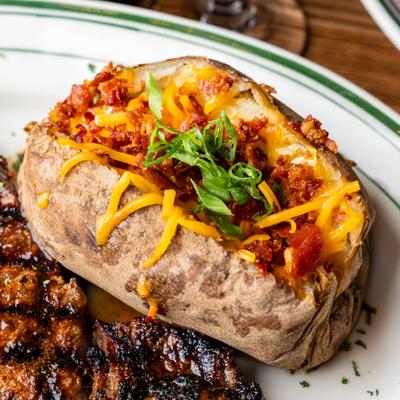 Loaded baked potato topped with bacon bits, cheese, and scallions, served with a steak.