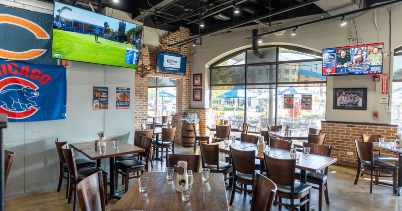 Sports bar interior with wooden tables, chairs, TVs, and large windows.