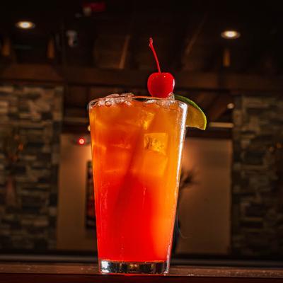 A glass of blood orange margarita, garnished with a cherry and a lime wedge.