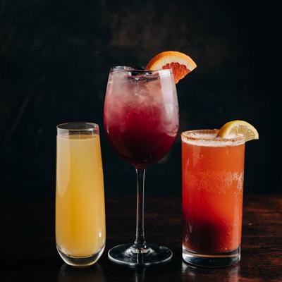 Three distinct cocktails line up on a dark table.