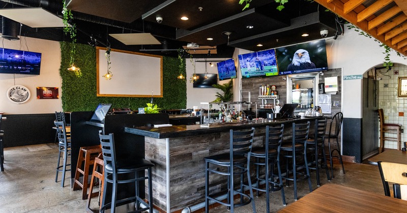 Interior, bar with an L-shaped counter, bar stools, wall-mounted TVs, green foliage decor