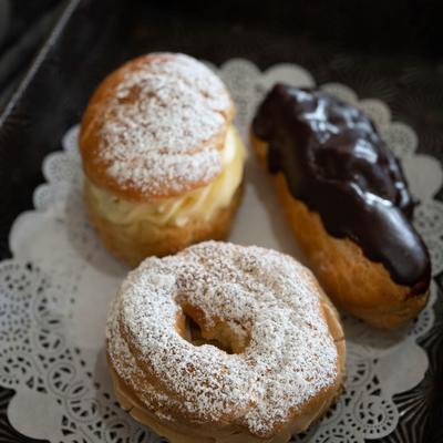 A tray with a lace doily holds three pastries, a cream puff, a choux, and an eclair.