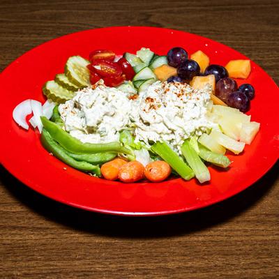 Assorted fresh vegetables and fruits topped with chicken salad on a red plate.