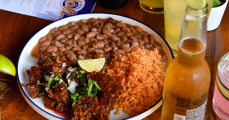 Plate of birria with rice and beans, alongside bottle of beer