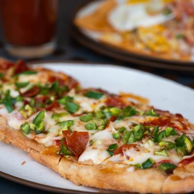 Flatbread topped with melted cheese, pepperoni, sliced jalapenos, and green onions.