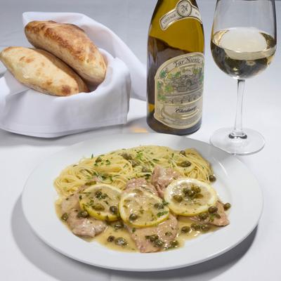 Veal Picatta served alogside basket of bread and bottle of white wine with a glass.