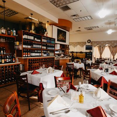 Arranged dining tables with tablecloths, set up for meal, wine racks and shelves.