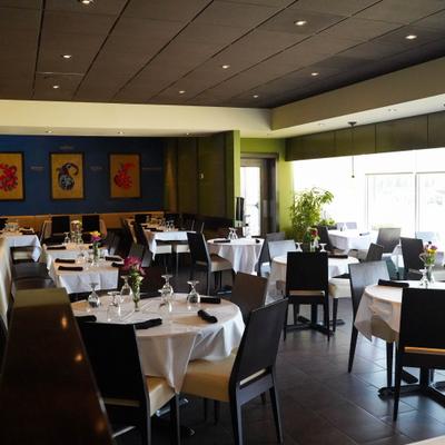 A modern restaurant interior with round tables, white tablecloths, and black chairs.