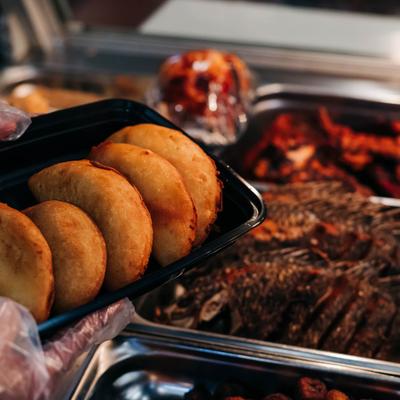 An employee presents a tray of empanadas in front of a to go food bar.