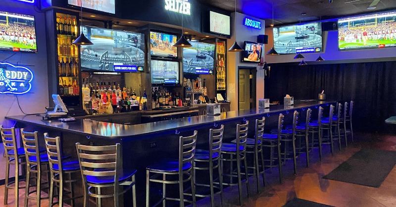 A bar with stools, neon lights, TVs, and bottles of liquor