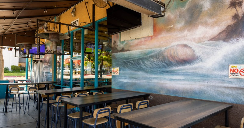 Outdoor seating area - high tables and chairs, featuring a mural of an ocean wave on the wall