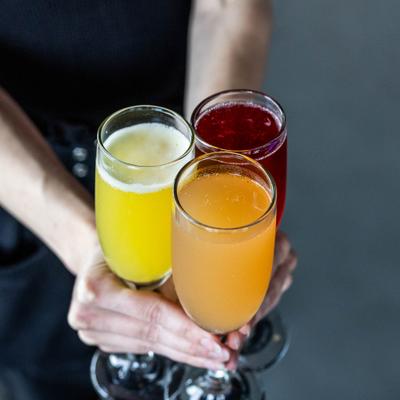 Person holding three glasses with various Mimosas.