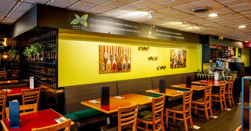 Interior with wooden tables, chairs, colorful spice artwork and greenery.
