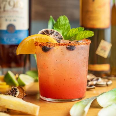 Pink cocktail garnished with orange and fresh mint.