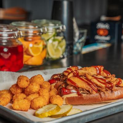 Hot dog topped with puled pork and fried onion petals, served with tater tots and pickles.