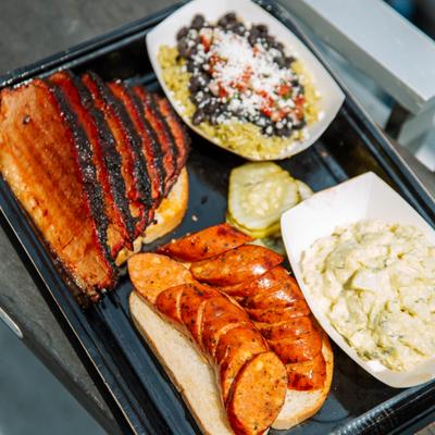 Sliced smoked brisket, sausage, potato salad, and black beans and rice on a tray.