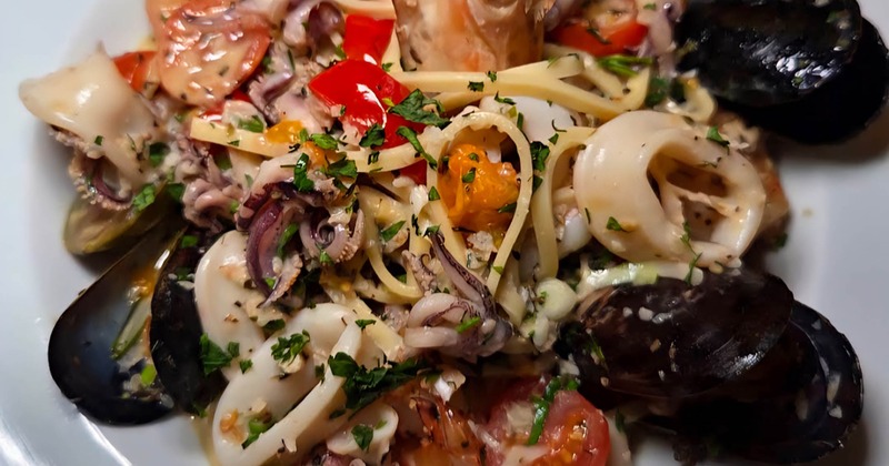 A plate of grilled shrimp served with a grilled lemon wedge and rosemary garnish
