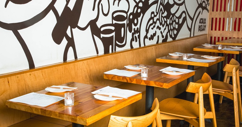 Interior of a restaurant with wooden tables and chairs, and a black and white mural on the wall