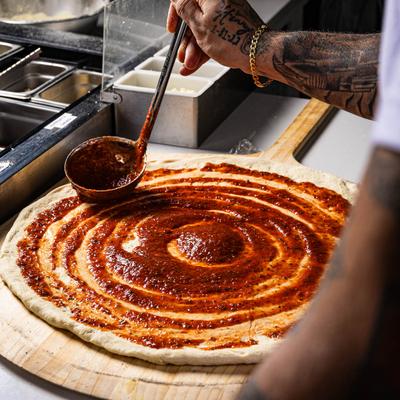 Pizza dough being topped with tomato sauce.