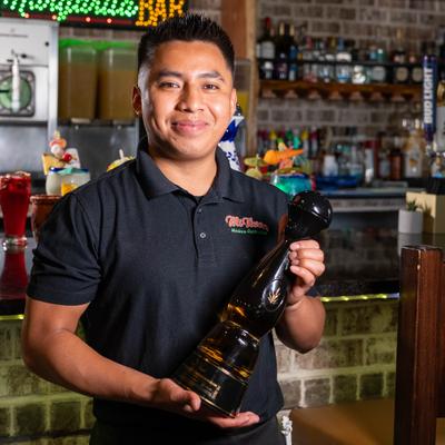 Bartender holding a bottle of tequila behind a bar.