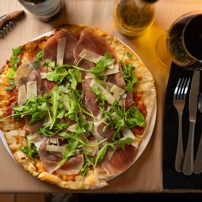 Prosciutto and arugula pizza topped with shaved Parmesan cheese.