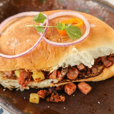 A sandwich filled with chorizo, carne asada, bacon, and and pineapple.