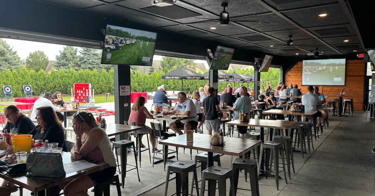 A covered patio with guests dining and TVs playing sports
