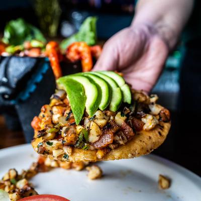 A hand holding a shrimp tostada topped with avocado slices.