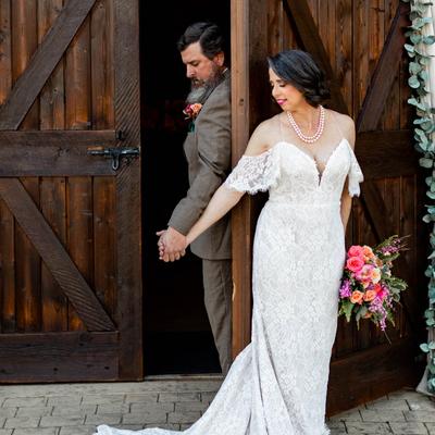 Elegant wedding couple holding hands at a wooden door entrance.