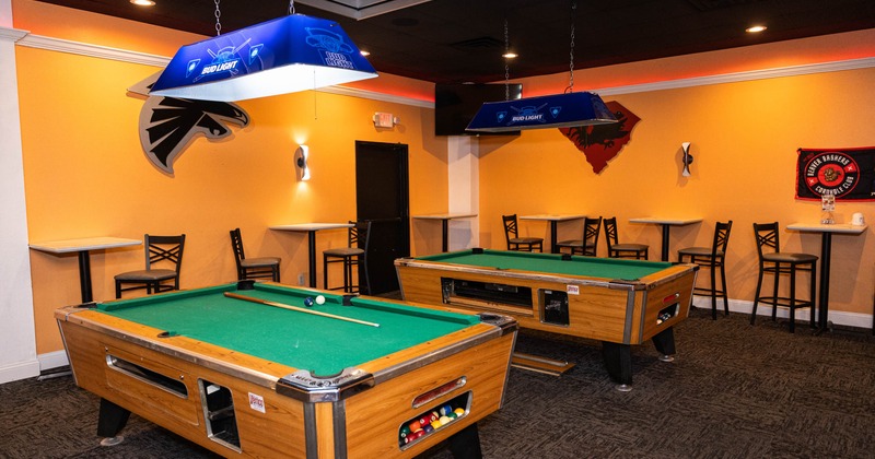 A recreational room with two billiard tables, high top tables and chairs