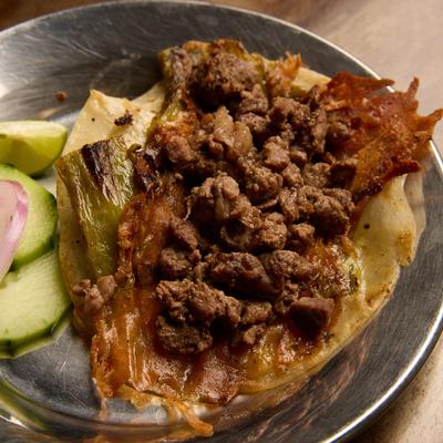 Steak taco, with grilled melted cheese, roasted green chile, cilantro, cabbage, and onions.