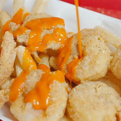 Serving of fried shrimp and fries being topped with sauce.