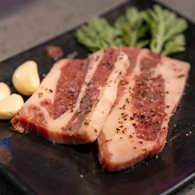 Raw pork belly slices seasoned with black pepper, served with raw garlic cloves and herbs.