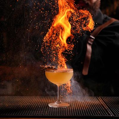Shot of a Cocktail flaming on bar counter with a bartender  in the back.