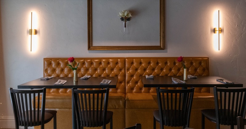 Interior, brown leather booth, two tables with red roses, black chairs and gold frame on the wall