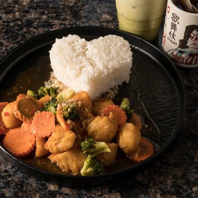 Heart-shaped rice with vegetables and tofu in brown sauce on a black plate.