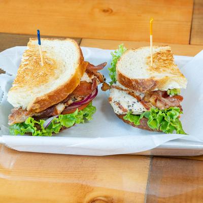 Grilled chicken sandwich with bacon, lettuce, and onions on toasted bread.