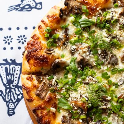 georgian cheesebread (khachapuri) with mushrooms and fresh herbs, pictured on blue and white traditional Georgian tablecloth