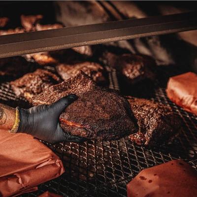 A hand lifting a charred piece of meat from a barbecue smoker.