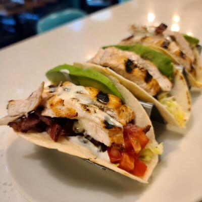 A close-up of three tacos with chicken, bacon, lettuce, tomato, avocado, and ranch..