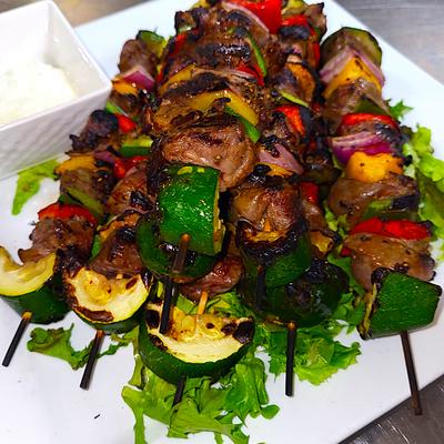 Grilled skewers with  meat and veggies, served on a white plate with a side of dip.