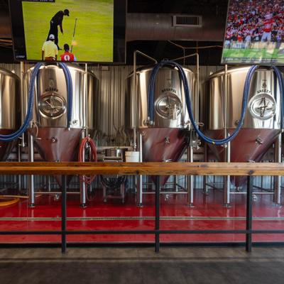Stainless brewing tanks behind a wooden counter with overhead TVs.