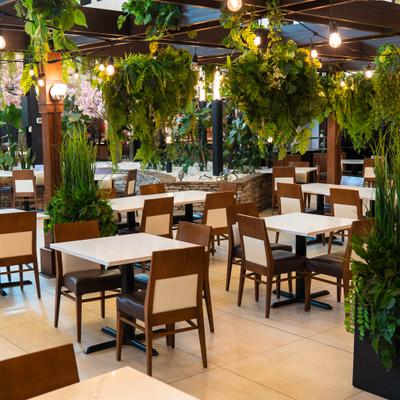 Outdoor dining patio with white tables, dark wood chairs, and hanging green plants.