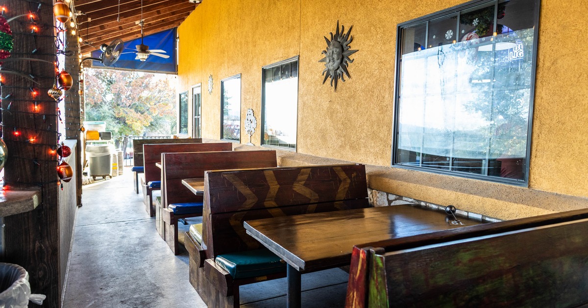 Outdoor restaurant seating area with wooden booths, blue cushions, and yellow stucco wall