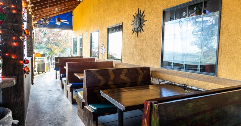 Outdoor restaurant seating area with wooden booths, blue cushions, and yellow stucco wall