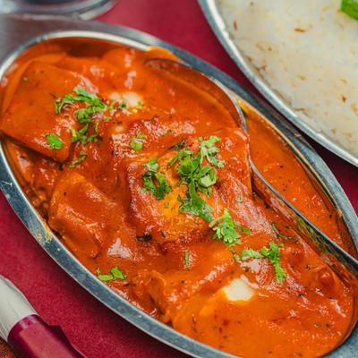 Butter chicken plate next to a plate with white rice, close up.