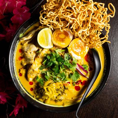 Spicy coconut curry ramen with chicken, boiled egg, crispy noodles, lime, and cilantro.