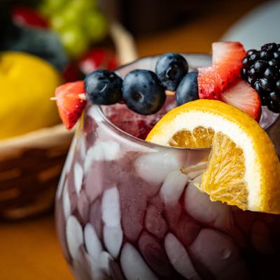 Close up of a red sangria glass, decorated with a berry skewer and a lemon slice.