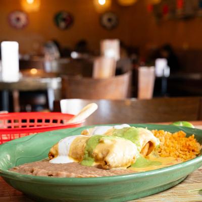 Two chimichangas topped with guacamole and sour cream, served with rice and beans.