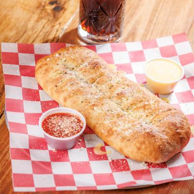 Garlic Cheese Bread on a red checkered paper with dipping sauce, and soda on a wooden table.